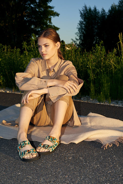 1. Woman wearing Omaking Meeliku Sandals in multicolor, sitting outdoors on a blanket