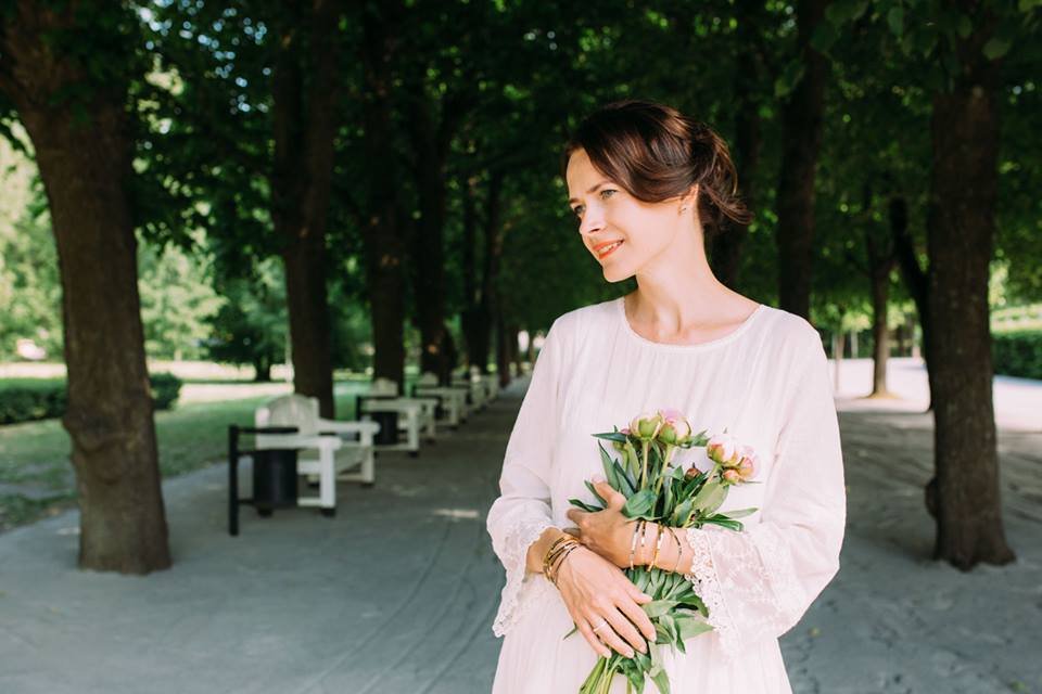 1. Woman in a park wearing Olla's MAAILMAN PARAS ÄITI bracelet in gold, holding flowers