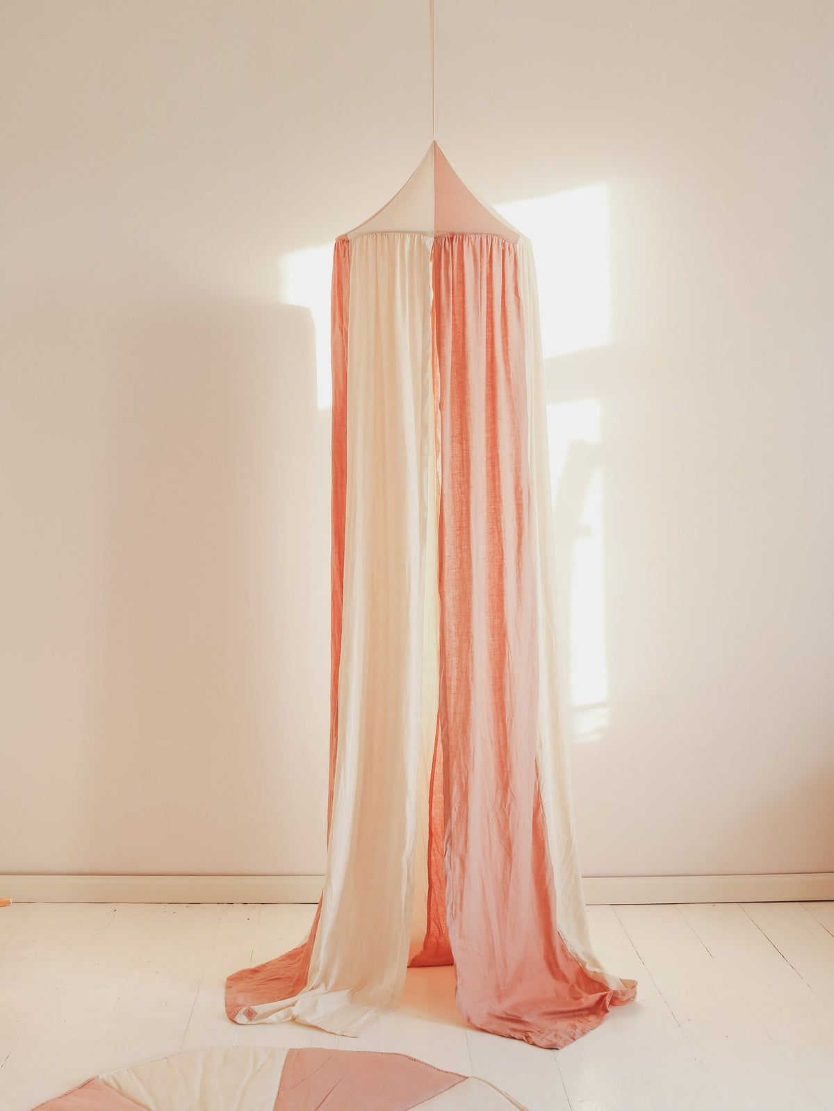 5. Powder pink and cream canopy hanging in a sunlit room, showcasing its elegant drape and soft fabric.
