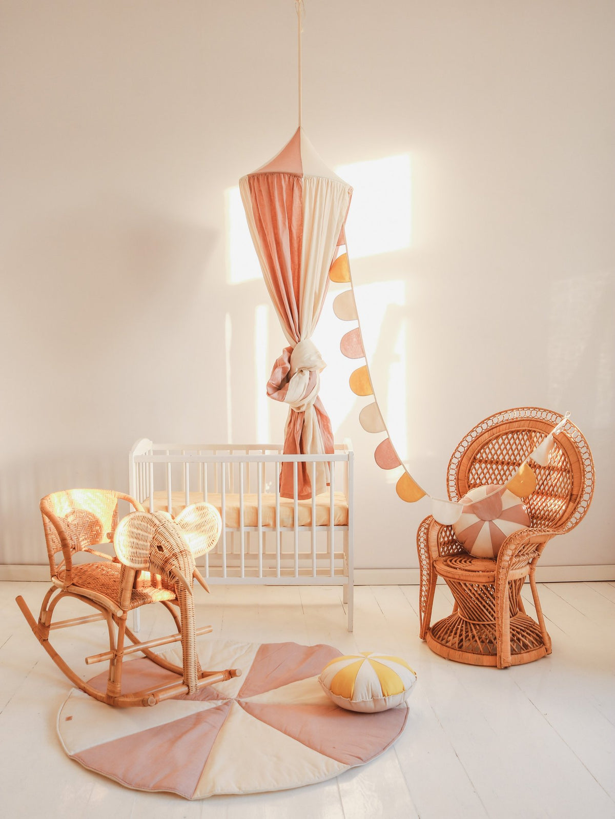 3. Powder pink and cream canopy in a nursery setting with a crib, wicker chair, and decorative garland, creating a playful and cozy space.