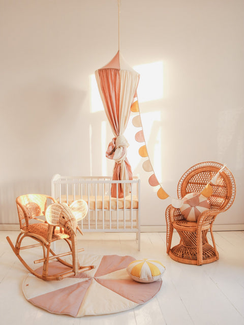 3. Powder pink and cream canopy in a nursery setting with a crib, wicker chair, and decorative garland, creating a playful and cozy space.