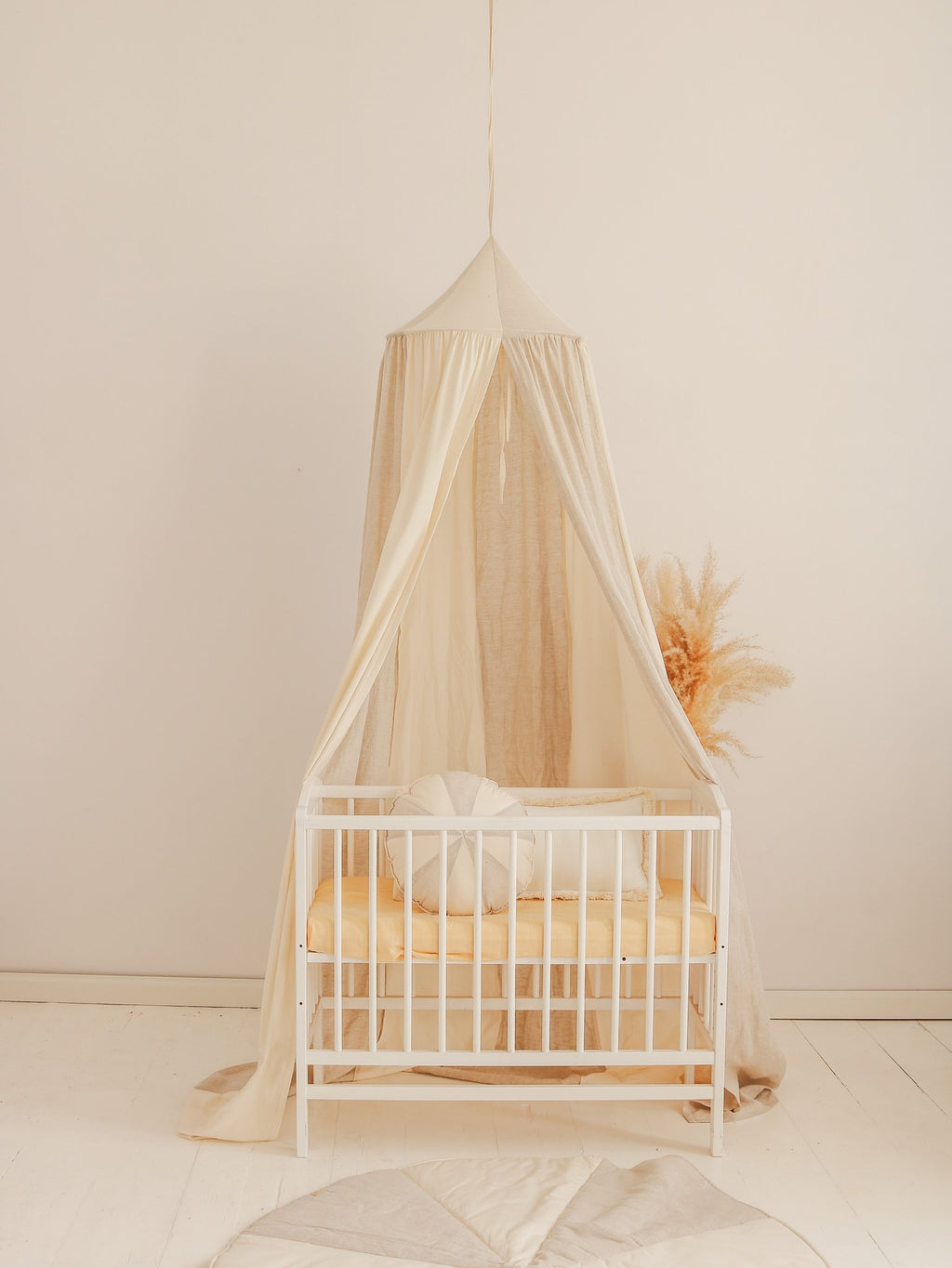 1. Cream canopy over white crib with beige bedding in a minimalist nursery setting