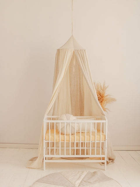 1. Cream canopy over white crib with beige bedding in a minimalist nursery setting