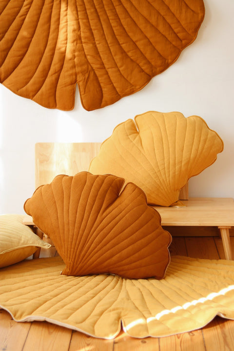 1. Lifestyle setting with caramel and yellow ginkgo leaf playmats and cushions in a cozy room, showcasing versatility and design