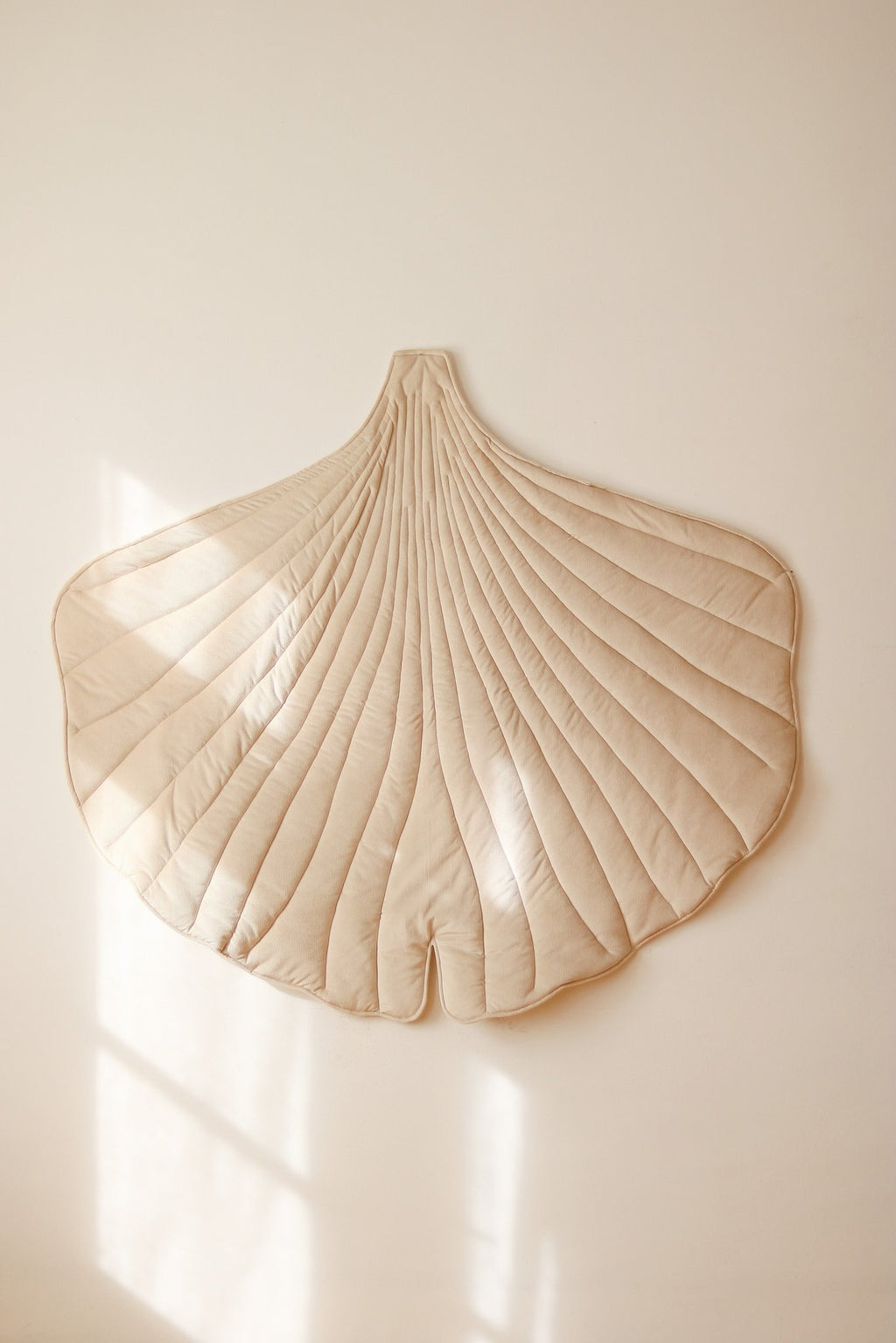 1. Cream ginkgo leaf playmat hanging on a wall in a bright room, showcasing its elegant quilted design and natural shape