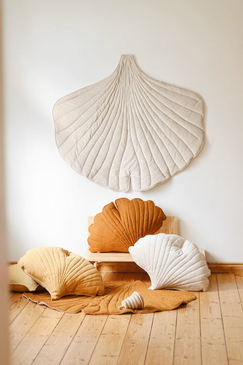 1. Cream ginkgo leaf playmat displayed on a wall with matching cushions in warm tones on a wooden floor, creating a cozy setting