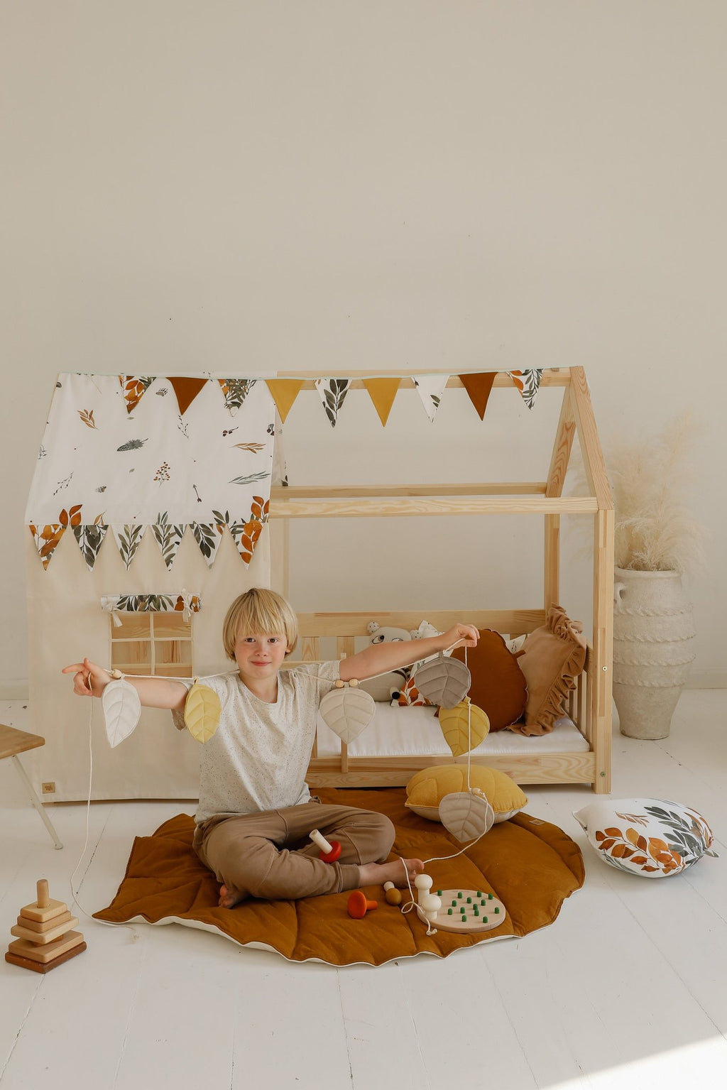 1. Child holding leaf garland sitting on caramel playmat in a playhouse