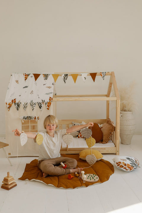 1. Child holding leaf garland sitting on caramel playmat in a playhouse