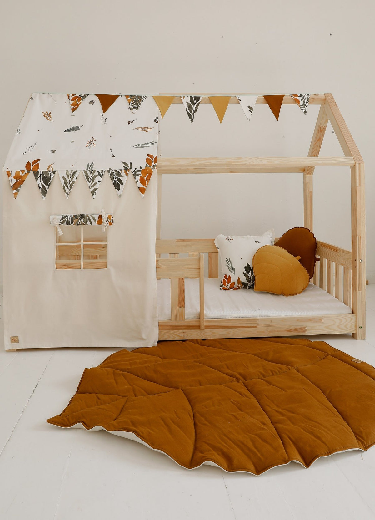 1. Wooden playhouse with caramel leaf playmat on the floor, decorated with bunting and cushions