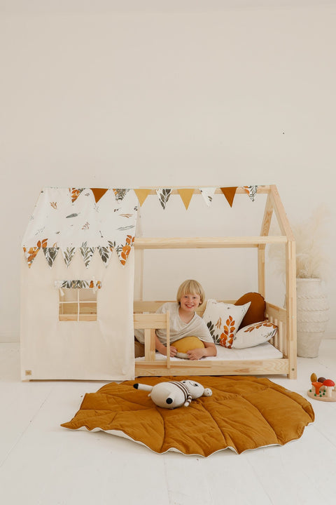 1. Child smiling in a wooden playhouse with caramel leaf playmat and toys