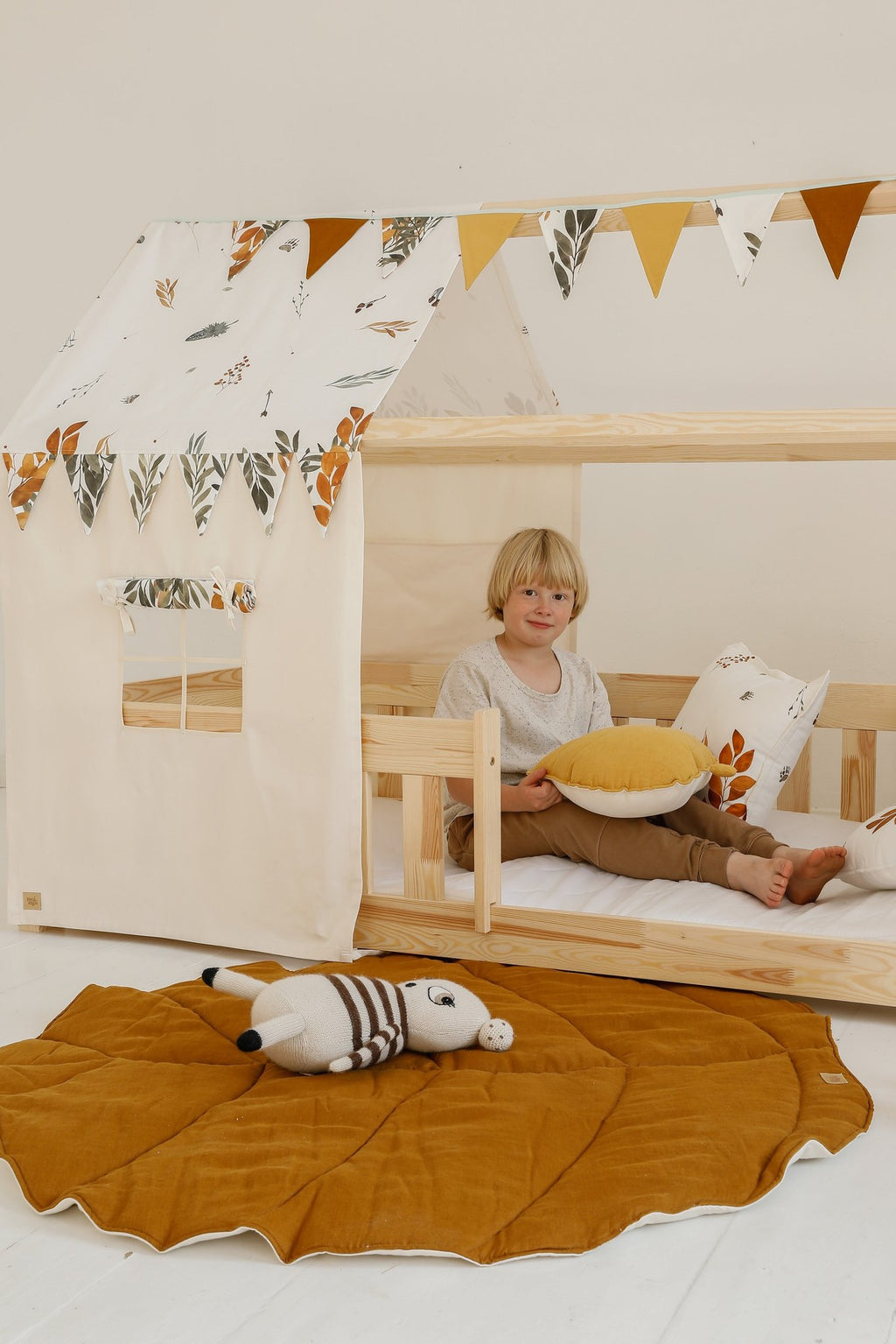 1. Child sitting in a wooden playhouse with caramel leaf playmat on the floor, surrounded by toys