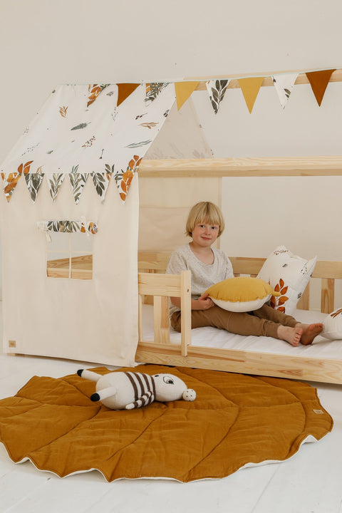 1. Child sitting in a wooden playhouse with caramel leaf playmat on the floor, surrounded by toys
