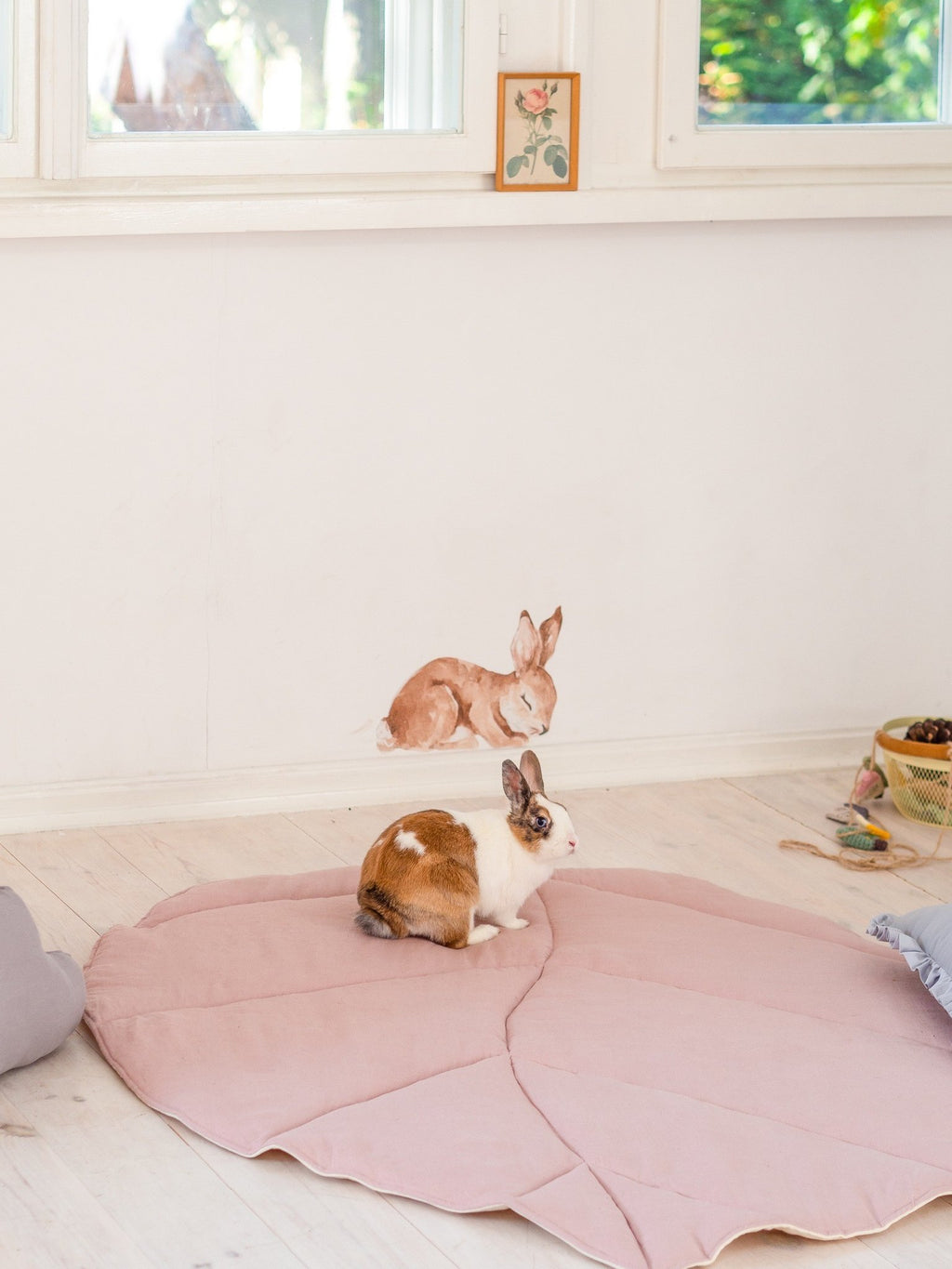 1. Rabbit sitting on powder pink leaf playmat in a bright room with wall art