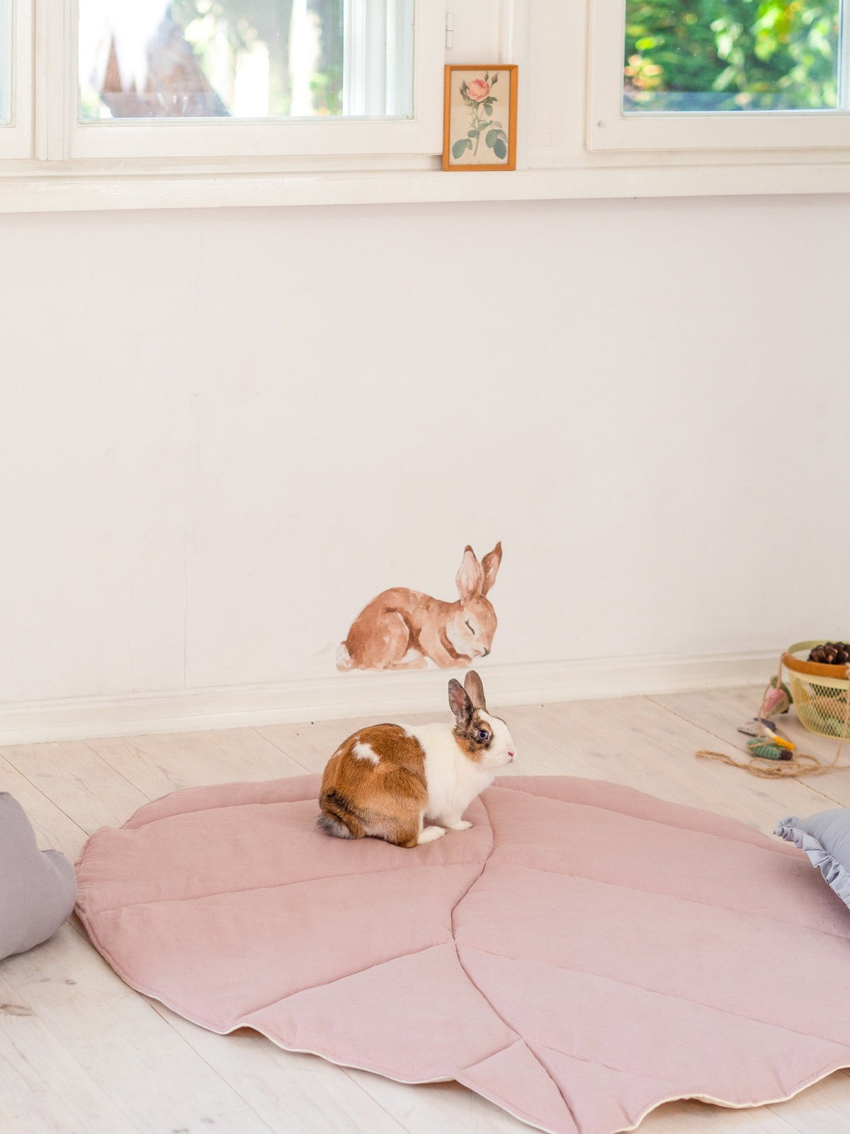 1. Rabbit sitting on powder pink leaf playmat in a bright room with wall art