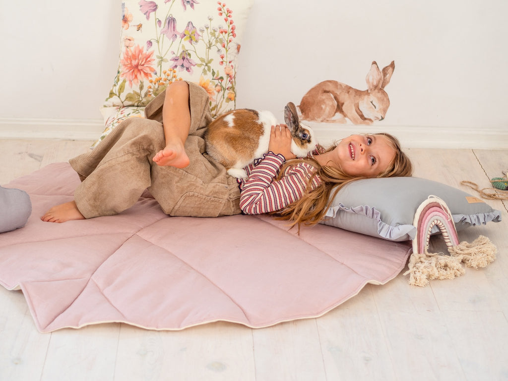 1. Girl lying on powder pink leaf playmat with a rabbit in a cozy room setting