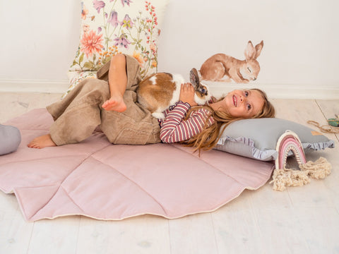 1. Girl lying on powder pink leaf playmat with a rabbit in a cozy room setting
