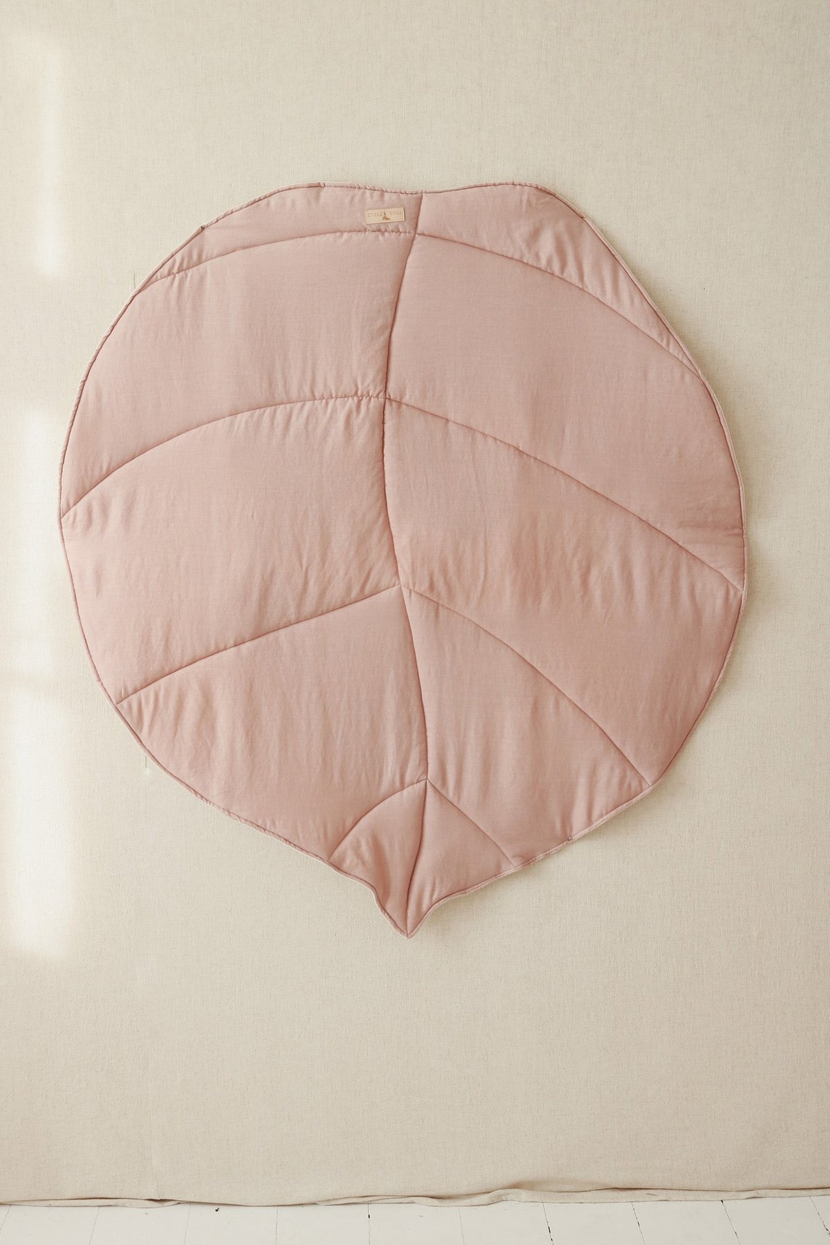 2. Powder pink ginkgo leaf-shaped playmat hanging against a neutral wall