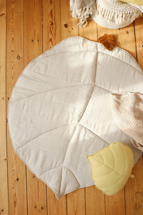 1. Organic cotton and linen leaf playmat in sand color on wooden floor with pillows, creating a cozy play area