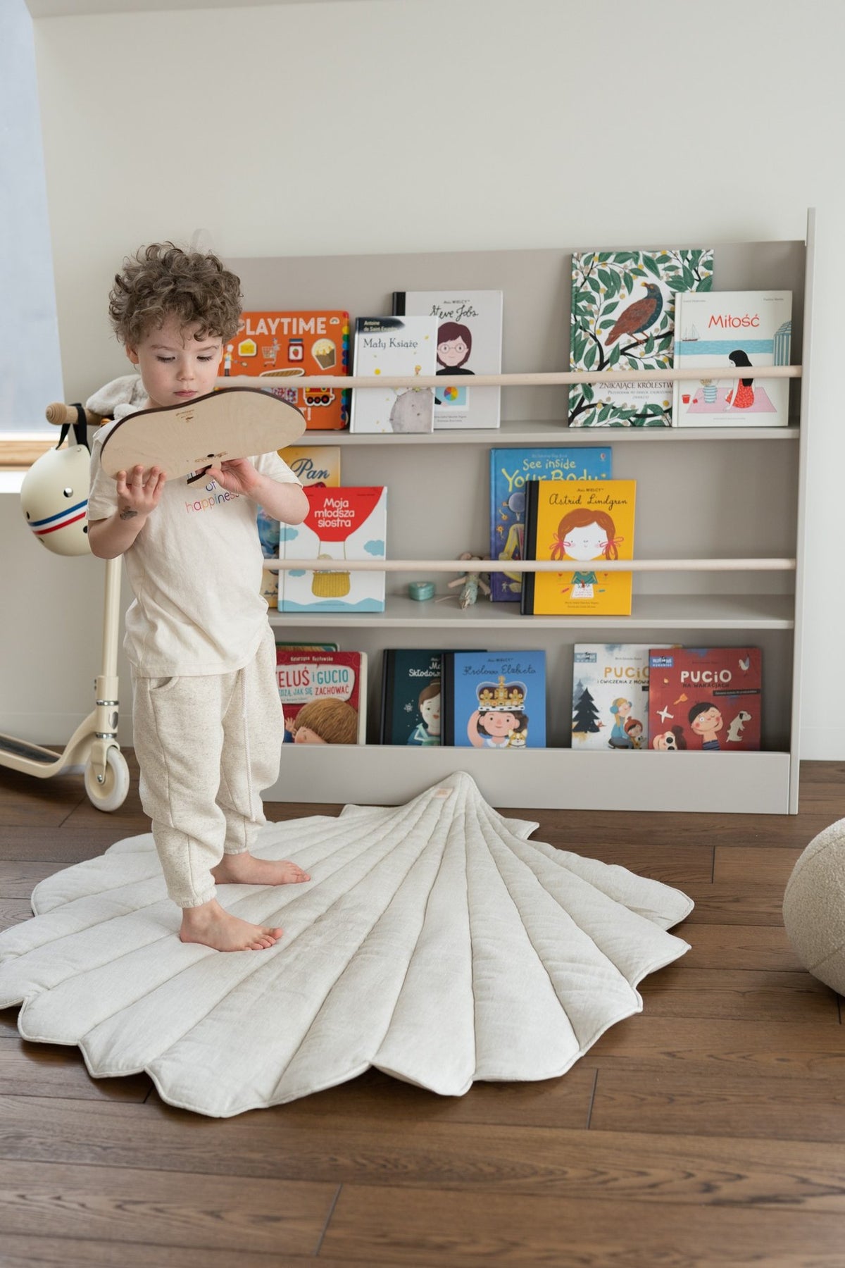 1. Child standing on organic cotton and linen shell playmat in sand color in a playroom with bookshelves