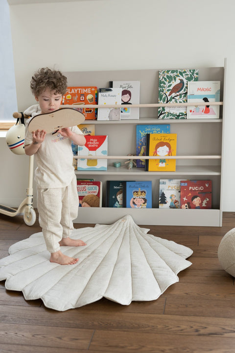 1. Child standing on organic cotton and linen shell playmat in sand color in a playroom with bookshelves