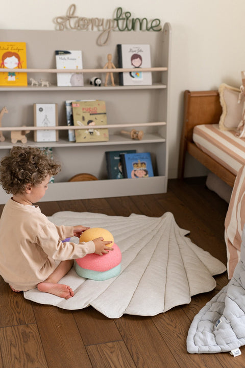 1. Child sitting on organic cotton and linen shell playmat in sand color in a playroom with bookshelves