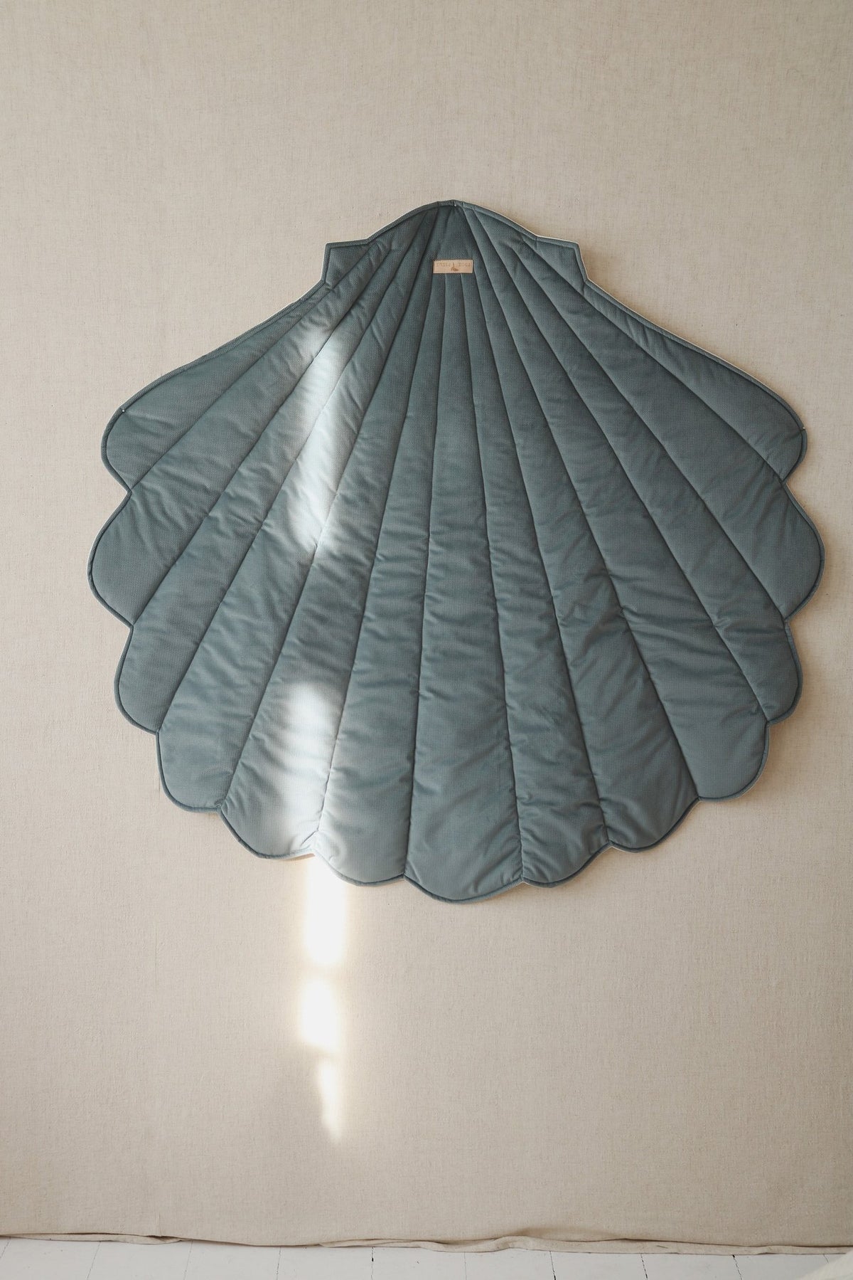 4. Blue shell-shaped playmat hanging on beige wall, showcasing versatile use as wall decoration