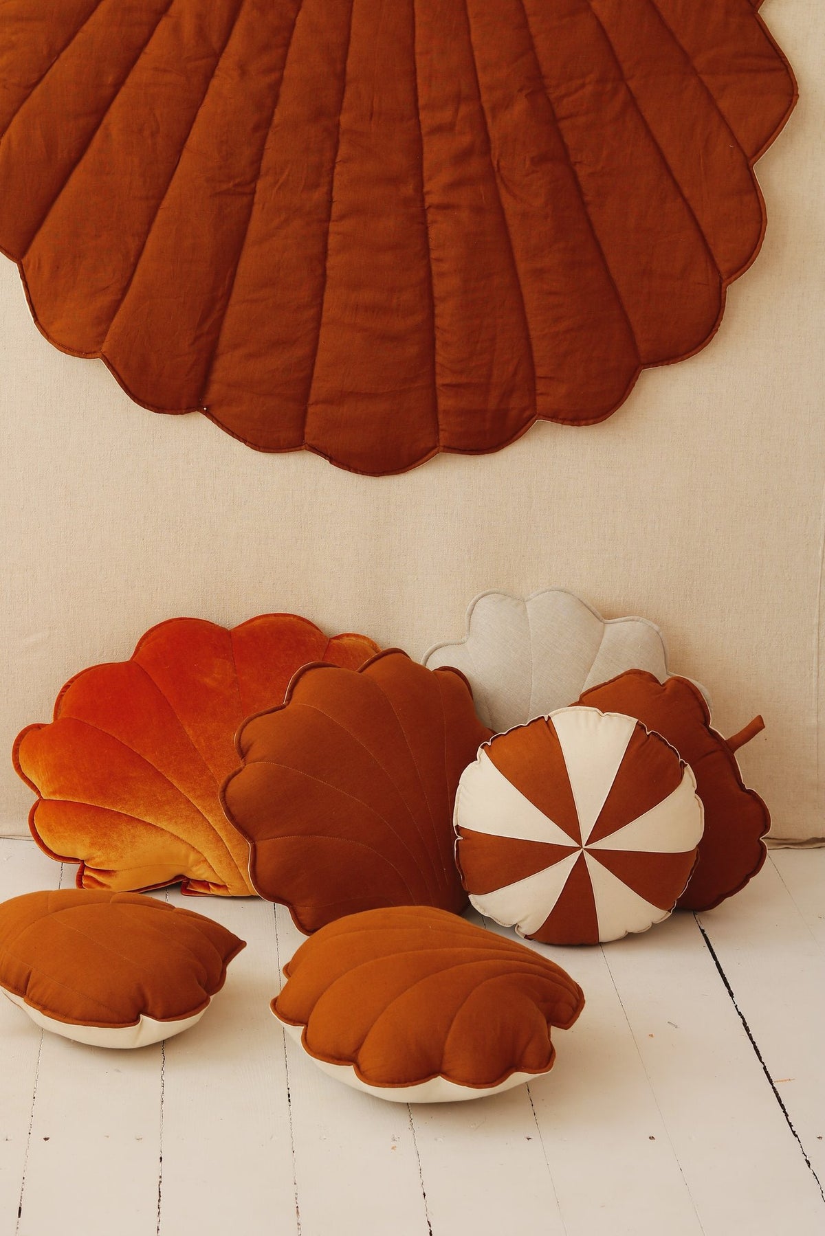 4. Flat lay of caramel shell playmat with assorted cushions in various shapes and colors on a white wooden floor