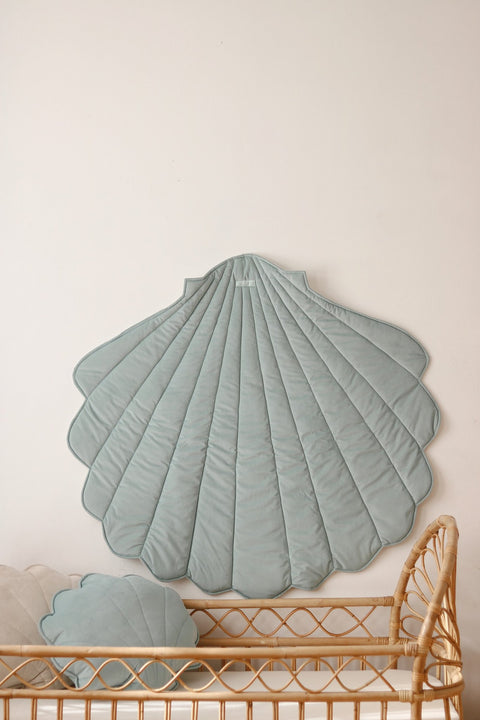 1. Mint green shell-shaped playmat hanging on wall above wicker crib in nursery setting