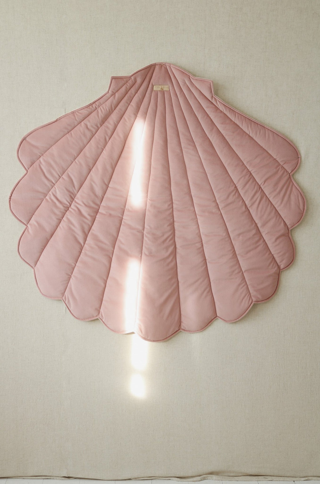 7. Powder pink shell playmat hanging on beige wall with sunlight