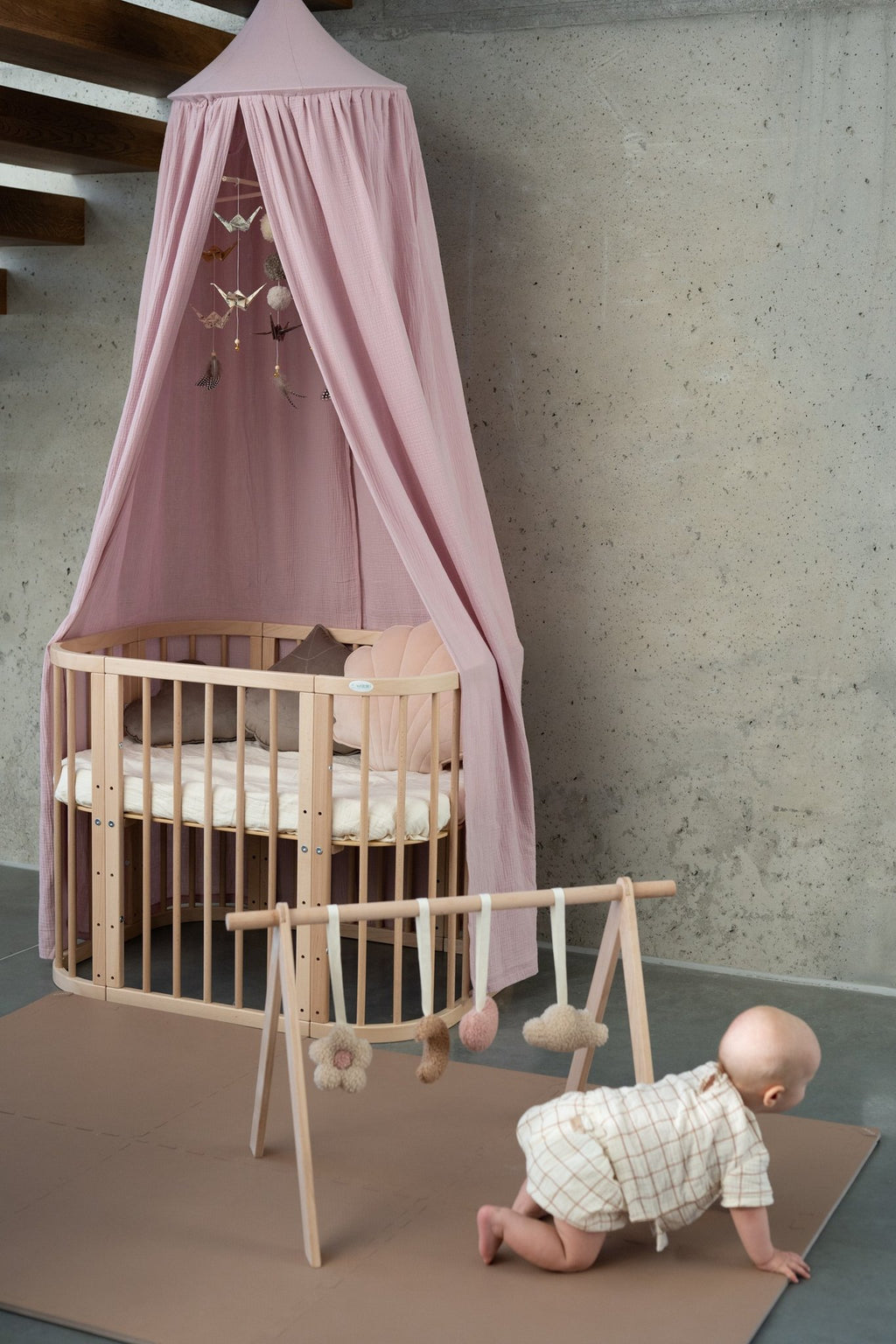 2. Baby crawling near crib with pink canopy and wooden play gym