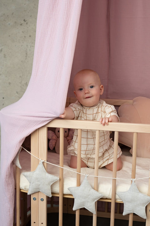 3. Baby sitting in crib under pink canopy with star garland