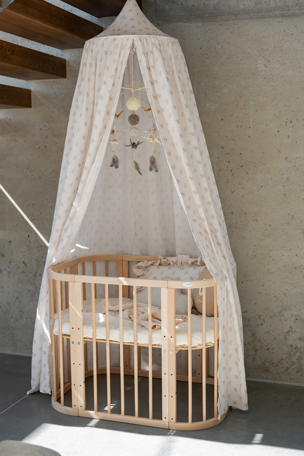 1. Beige boho floral canopy over wooden crib in modern room with concrete wall, featuring hanging ornaments