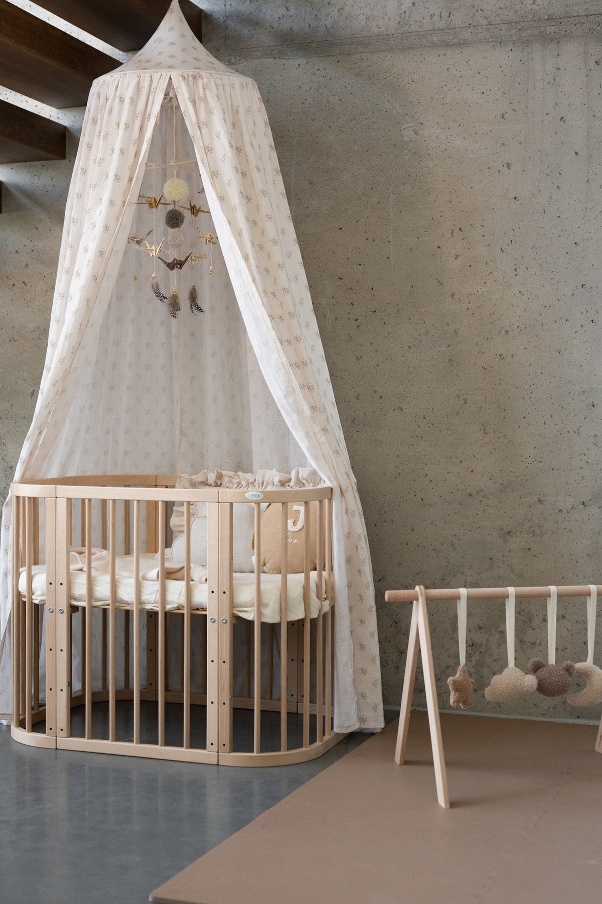 5. Beige floral canopy over wooden crib with play gym in modern room, concrete wall background