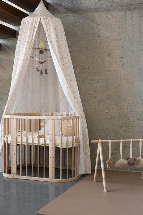5. Beige floral canopy over wooden crib with play gym in modern room, concrete wall background