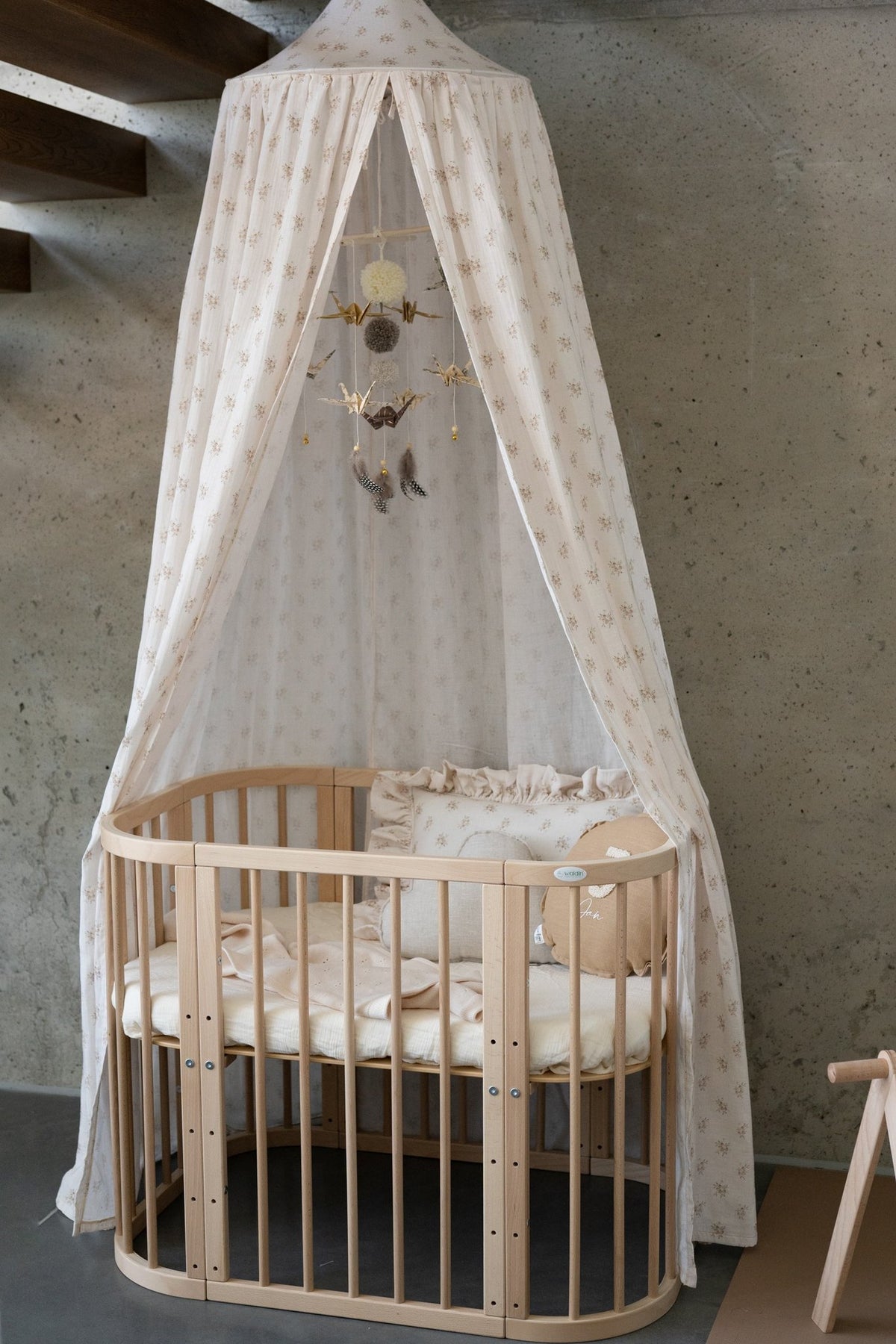 2. Studio shot of beige floral canopy over wooden crib with hanging decorations, set against concrete wall