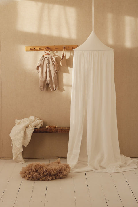 1. Cream cotton canopy in a nursery with hanging clothes and a bench, creating a peaceful atmosphere