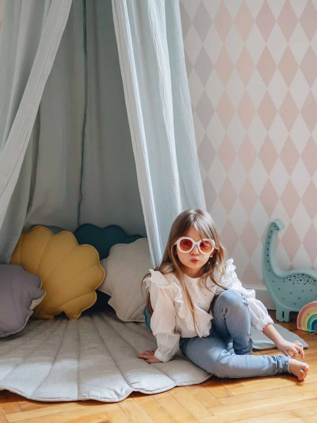 6. Young girl sitting under mint green canopy with colorful pillows in a playful room