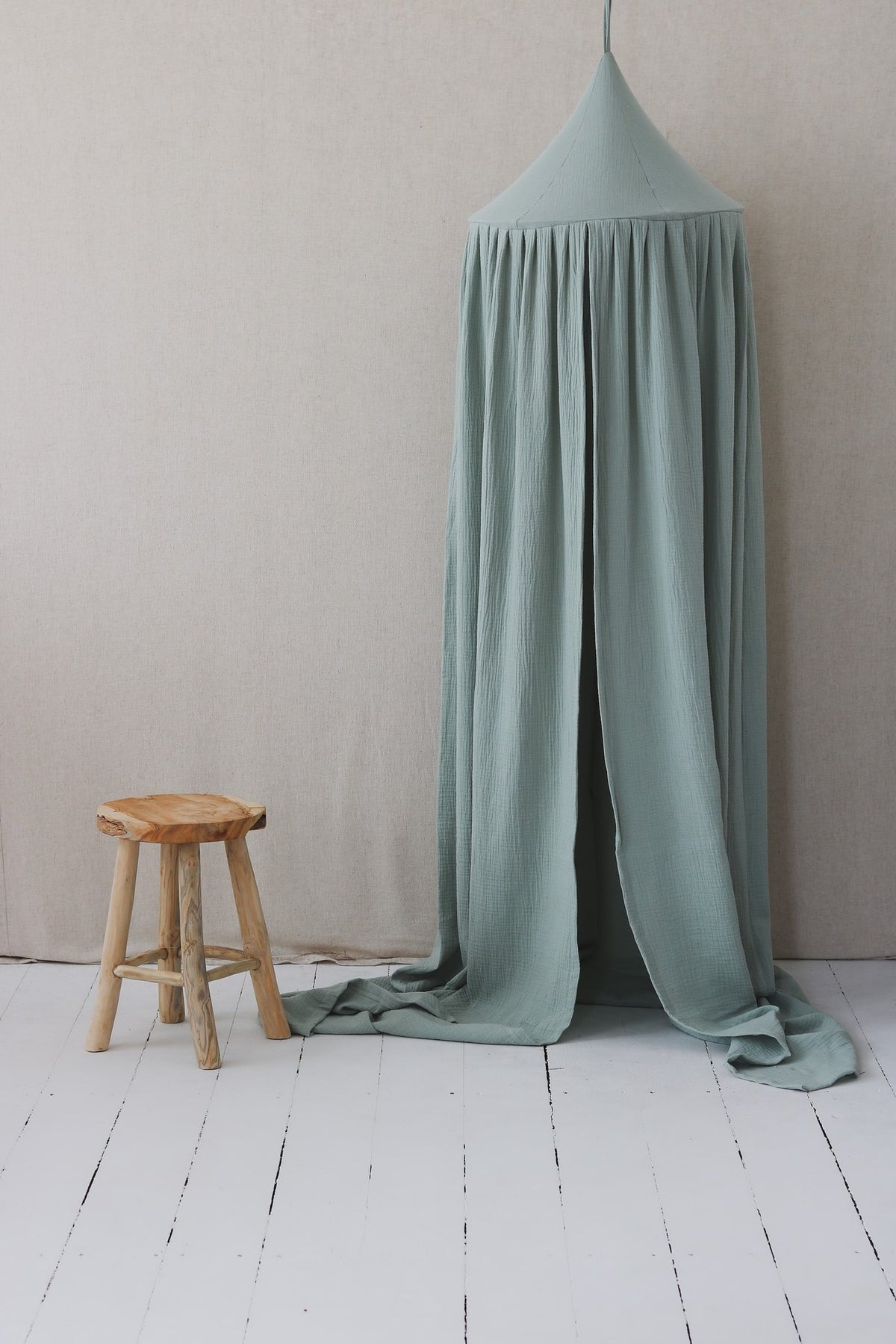 3. Mint green cotton canopy next to a wooden stool in a minimalist room