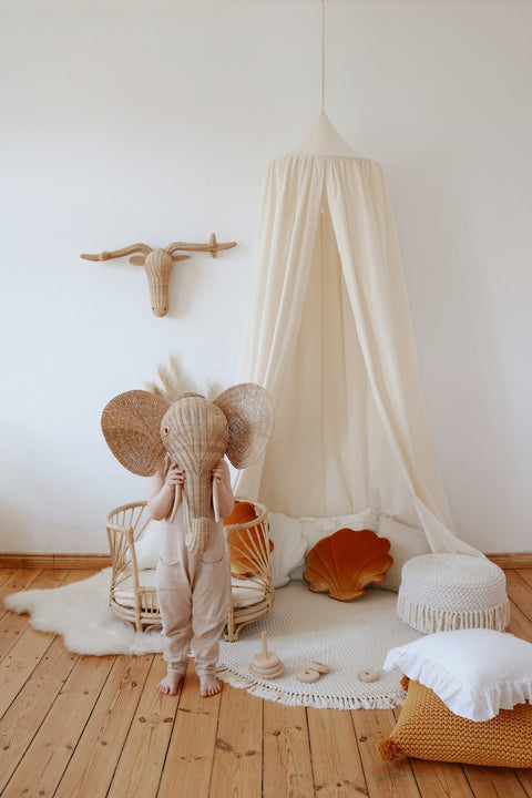3. Child with elephant mask in playroom featuring organic cotton canopy and rattan decor