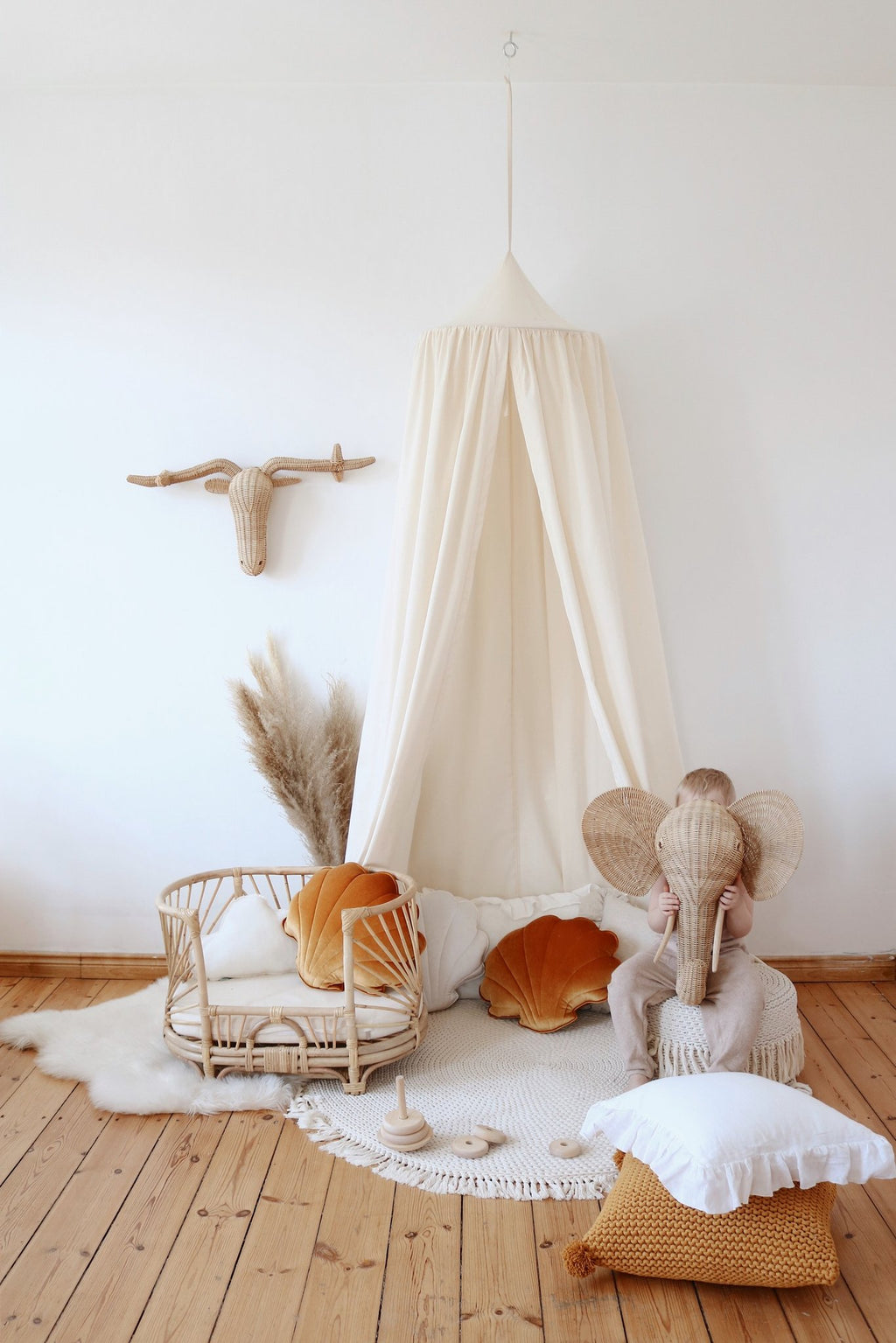 1. Child in beige outfit with elephant mask in room with organic cotton canopy and rattan furniture