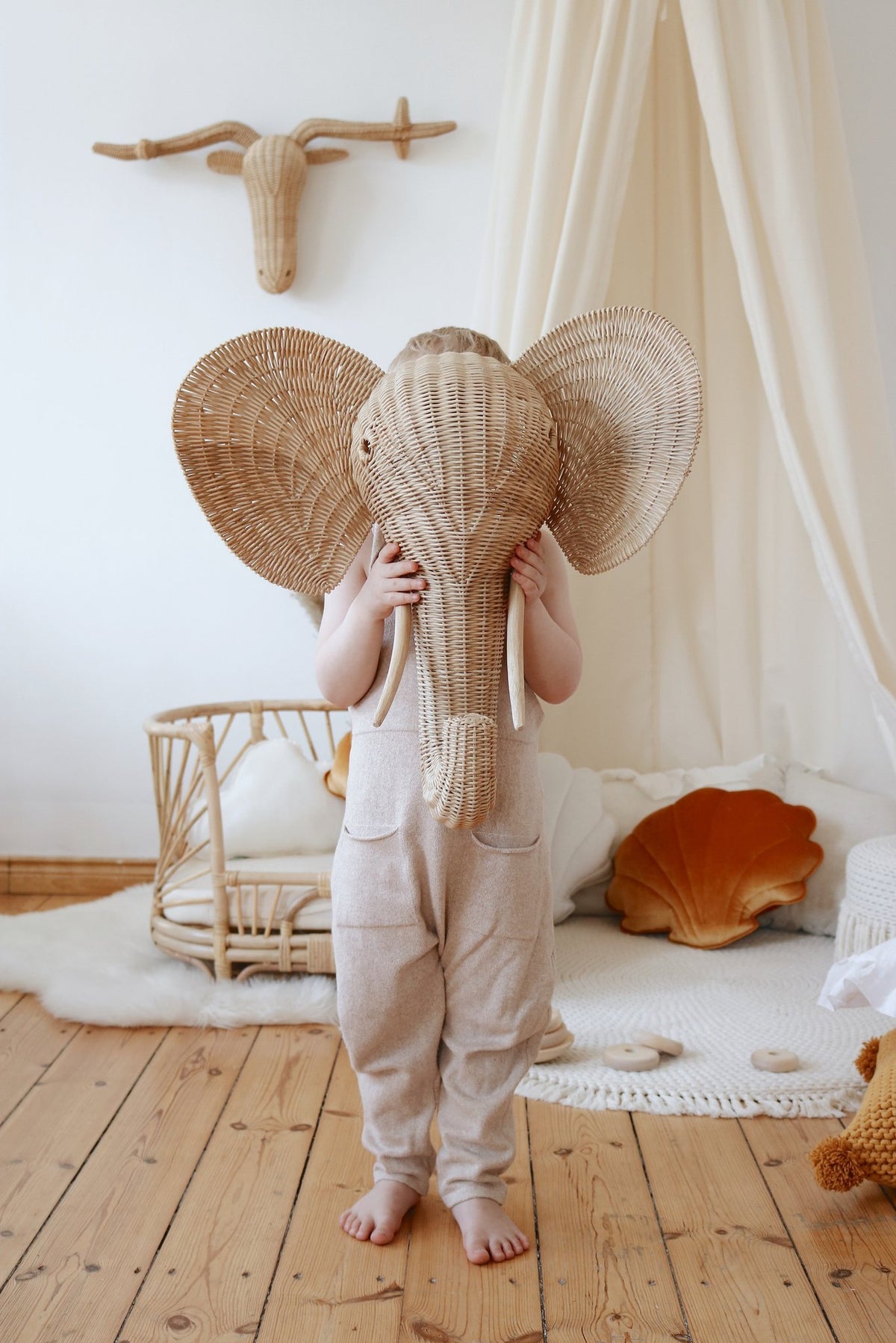 9. Child in beige outfit with elephant mask in room with organic cotton canopy and rattan furniture