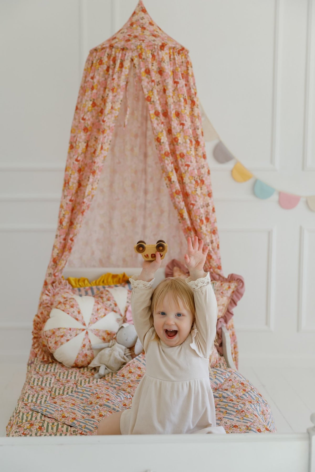 17. Girl standing under floral canopy with cushions and garland in a bright room