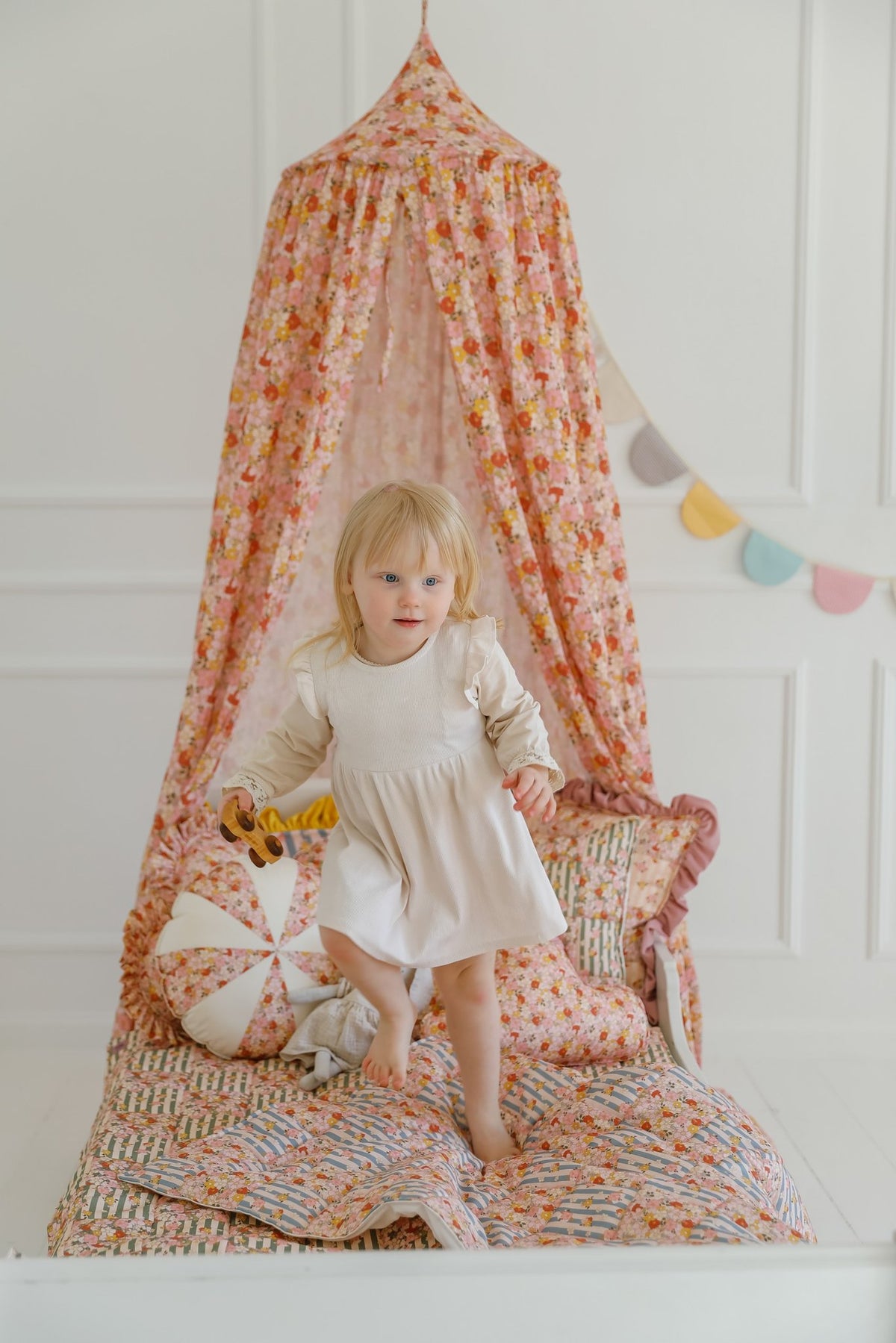 14. Girl standing under floral canopy with cushions and garland in a bright room