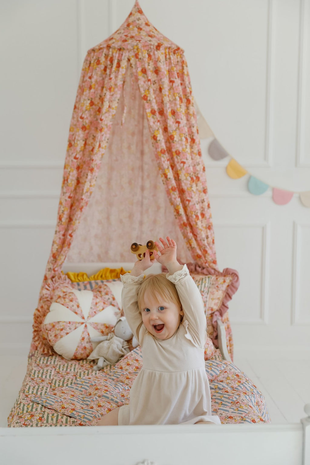 12. Girl standing under floral canopy with cushions and garland in a bright room