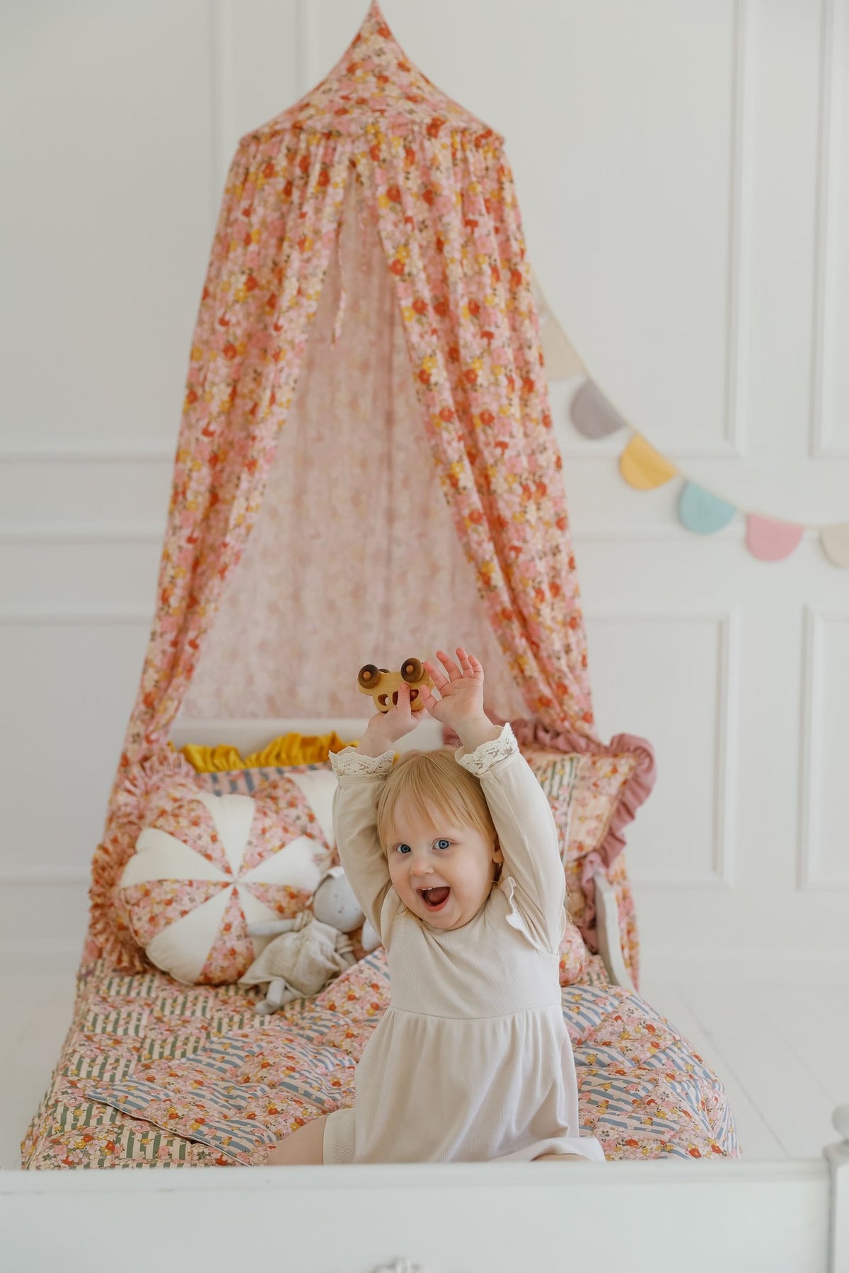 12. Girl standing under floral canopy with cushions and garland in a bright room