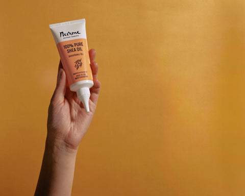 1. Hand holding Nurme 100% Pure Shea Oil twist cap tube against orange background
