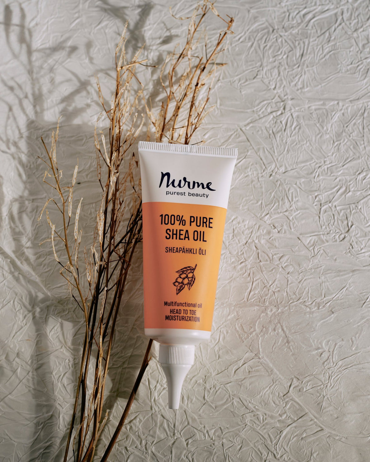 2. Nurme 100% Pure Shea Oil twist cap tube standing upright with dried plants on textured surface
