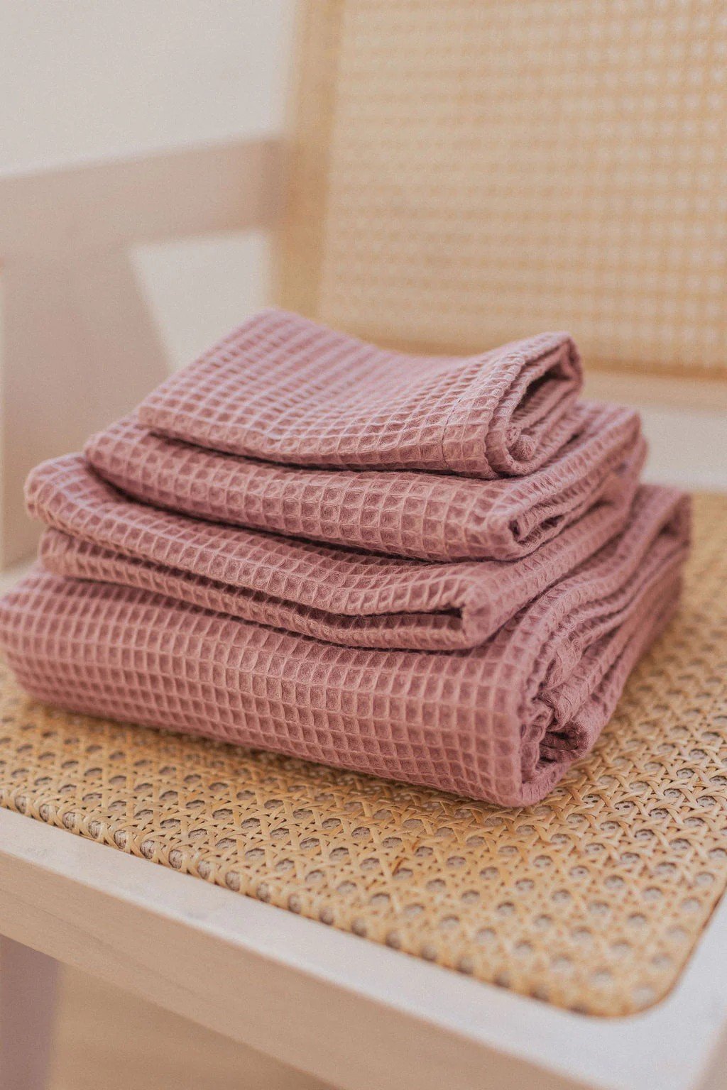 1. Stack of old pink waffle cotton towels on a woven chair, showcasing texture and color