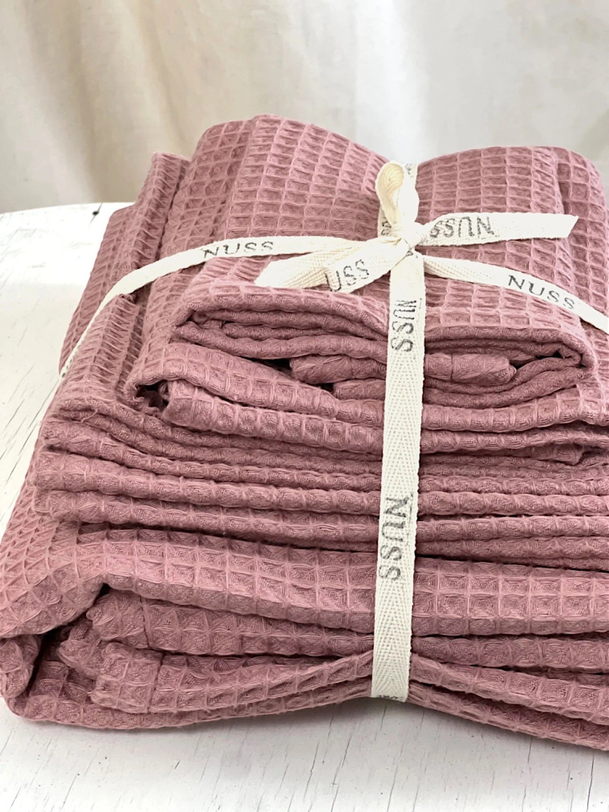 2. Set of old pink waffle cotton towels tied with Nuss branded ribbon on a white surface