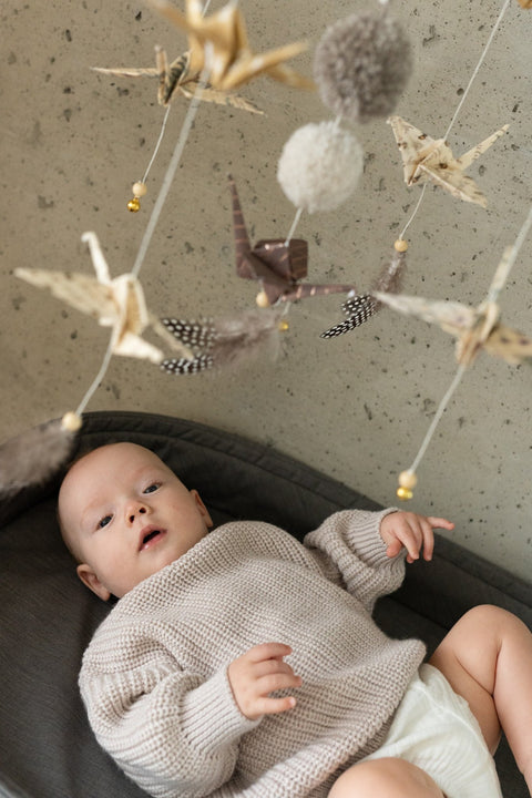 4. Close-up of baby reaching towards Moi Mili origami mobile with paper cranes and pompoms